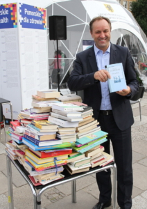 Marszałek województwa pomorskiego Mieczysław Struk przy książkach zbieranych dla pacjentów pomorskich szpitali